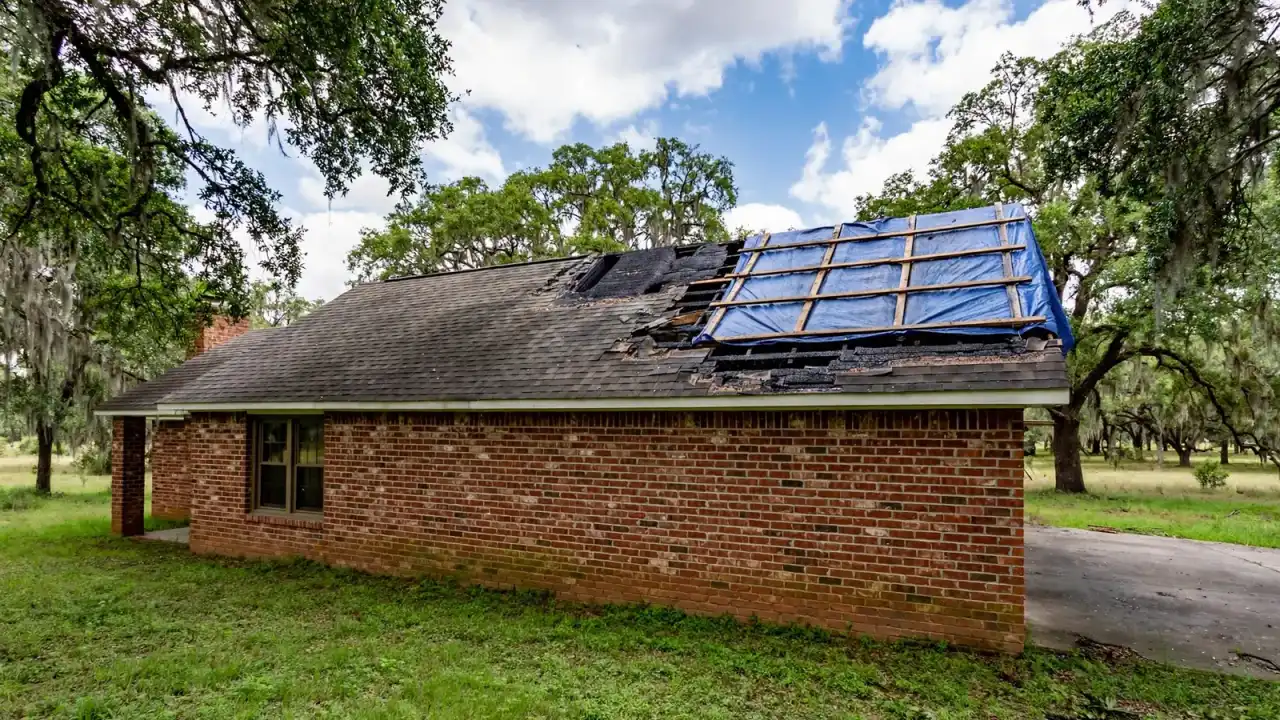 Blue tarp held down with wood battens over a burned section of a shingle roof